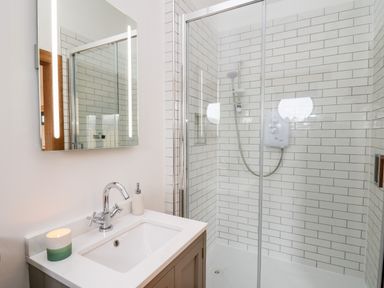 A bathroom with a sink and mirror next to a glass enclosed shower with white subway tiles at Tin Shed in Nantmel near Rhayader