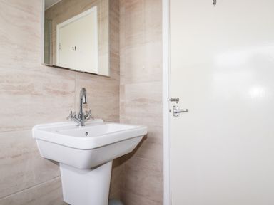A bathroom sink with a mirror above and a closed white door to the right at Sandpiper in Perranporth
