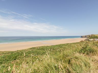 A sandy beach and ocean viewed from a grassy cliff at Sandpiper in Perranporth