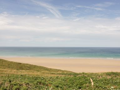 A sandy beach with ocean waves and grassy dunes under a cloudy sky at Sandpiper in Perranporth