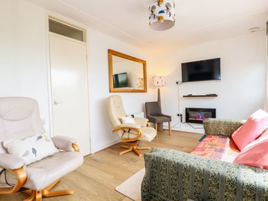 A living room with an armchair a sofa a wall mirror a television and a floor lamp at Sandpiper in Perranporth