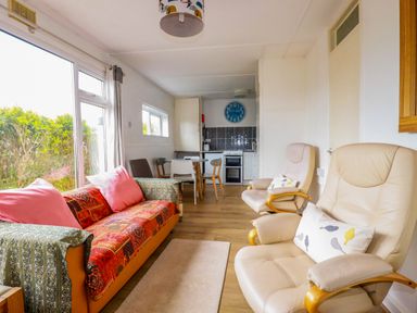 A living room with a sofa and armchairs next to a dining table and kitchen at Sandpiper in Perranporth