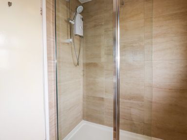 A shower area with beige tiled walls and a white electric shower unit at Sandpiper in Perranporth