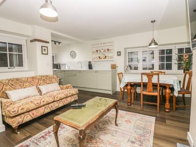 A living room with a patterned sofa a wooden coffee table and a dining table with chairs at Church How Cottage in Nether Wasdale