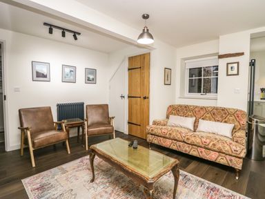 A living room with patterned sofa two brown chairs glass coffee table and framed pictures on the wall at Church How Cottage in Nether Wasdale