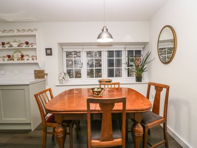 A dining area with a wooden table and four chairs near a window with a stone wall outside at Church How Cottage in Nether Wasdale