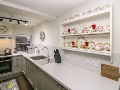 A kitchen with a countertop sink, knife block, microwave, kettle, oven, and shelves holding china at Church How Cottage in Nether Wasdale