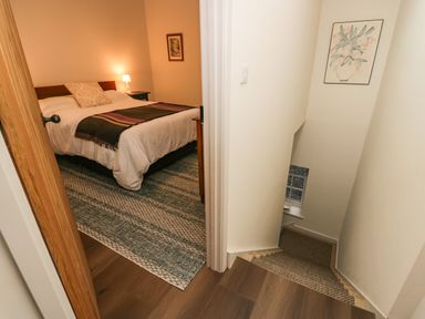 A bedroom with a bed lamp and framed picture next to a stairway with a carpet and a wall painting at Church How Cottage in Nether Wasdale