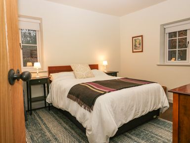 A bedroom with a double bed bedside tables with lamps windows and a framed picture on the wall at Church How Cottage in Nether Wasdale