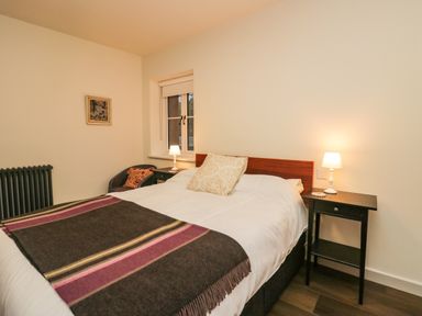 A bedroom with a double bed two bedside tables with lamps a window a chair and a framed picture on the wall at Church How Cottage in Nether Wasdale