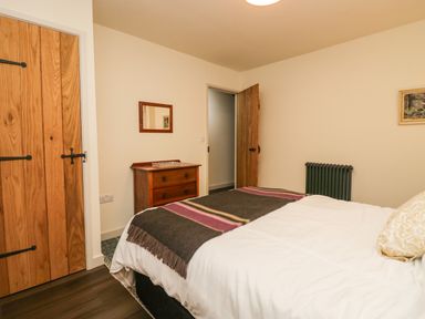 A bedroom with a bed with white bedding and a striped blanket a wooden dresser a wooden door a closet with wooden doors and a radiator at Church How Cottage in Nether Wasdale