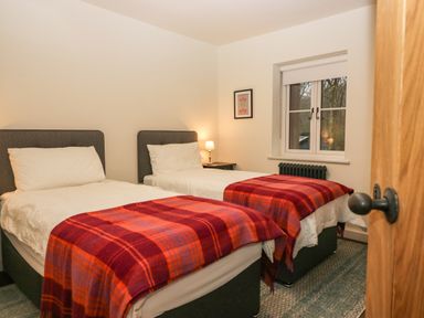A bedroom with two single beds with red plaid blankets a window and a nightstand with a lamp at Church How Cottage in Nether Wasdale
