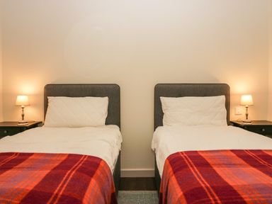A bedroom with two single beds with white bedding and red plaid blankets at Church How Cottage in Nether Wasdale