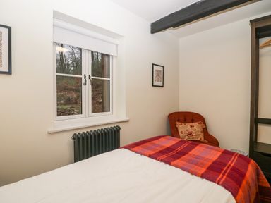 A bedroom with a bed covered by a red and orange plaid blanket a red chair with a pillow a window and a black radiator at Church How Cottage in Nether Wasdale