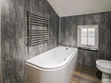 A bathroom with a bathtub, towel radiator, window, and toilet at Church How Cottage in Nether Wasdale