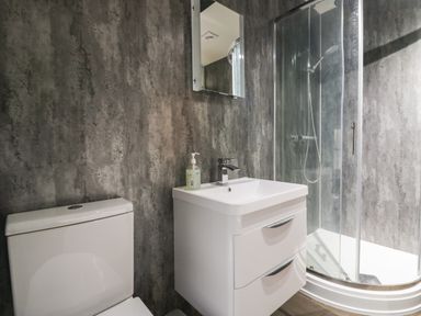 A bathroom with a toilet a sink with a cabinet a mirror and a curved glass shower enclosure at Church How Cottage in Nether Wasdale