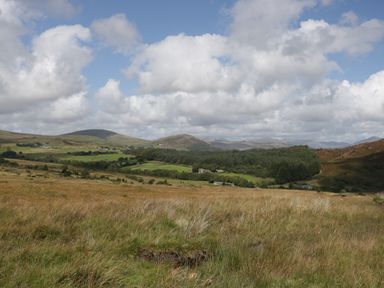 A landscape with grassy fields hills and trees under a cloudy sky at Church How Cottage in Nether Wasdale