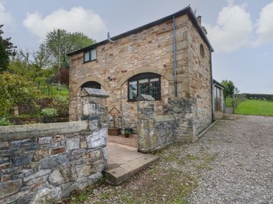 A stone building with arched windows and a stone wall gate at The Coach House in Trelogan Hall Trelogan near Trelawnyd