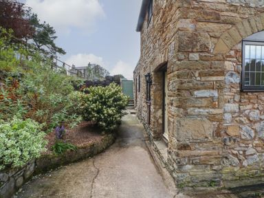 A stone building next to a paved pathway with plants and shrubs alongside at The Coach House in Trelogan Hall Trelogan near Trelawnyd
