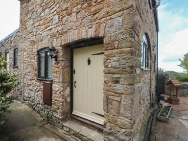 A stone exterior wall with a cream door and windows next to a flower bed and a wish well at The Coach House Trelogan Hall Trelogan near Trelawnyd