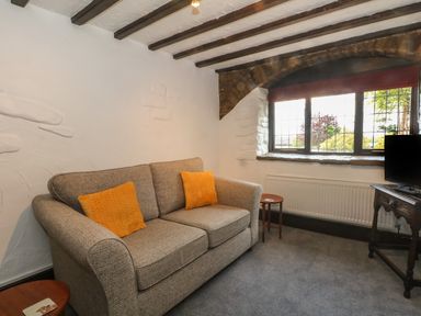 A living room with a sofa two orange cushions side tables and a window at The Coach House Trelogan Hall Trelogan near Trelawnyd
