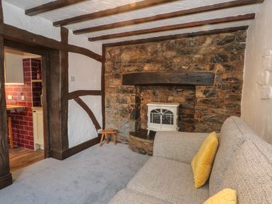 A sitting room with a stone fireplace a small white stove a grey sofa with yellow cushions and exposed wooden beams at The Coach House Trelogan Hall Trelogan near Trelawnyd