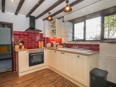A kitchen with cream cabinets red tiled backsplash oven sink and window at The Coach House Trelogan Hall Trelogan near Trelawnyd