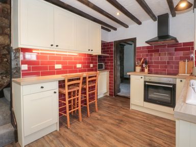 A kitchen with wooden floor cabinets and red tiled walls with two wooden chairs at The Coach House Trelogan Hall Trelogan near Trelawnyd