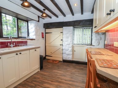 A kitchen with cream cabinets wooden chairs and a wooden floor at The Coach House Trelogan Hall Trelogan near Trelawnyd