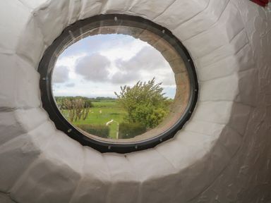 A round window with a view of green fields trees and a cloudy sky at The Coach House in Trelogan Hall Trelogan near Trelawnyd