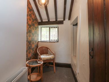 A small room with a wicker chair and glass top table under a window with wooden beams on the ceiling at The Coach House in Trelogan Hall Trelogan near Trelawnyd