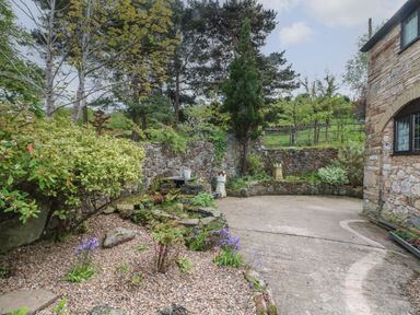 A garden area with gravel, plants, and a stone wall next to a stone building at The Coach House in Trelogan Hall Trelogan near Trelawnyd