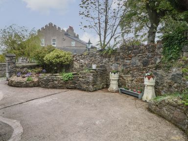 A stone garden wall with plants and flower pots on a paved area at The Coach House Trelogan Hall Trelogan near Trelawnyd