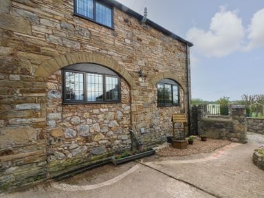 A stone exterior wall with two arched windows a flower planter and a wooden decorative well at The Coach House in Trelogan Hall Trelogan near Trelawnyd