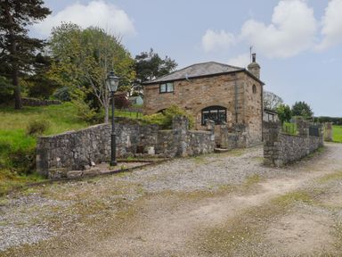 A stone house with a slate roof and stone wall along a gravel driveway at The Coach House in Trelogan Hall Trelogan near Trelawnyd