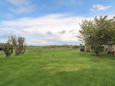A large green lawn with trimmed trees and a house partially visible at The Coach House in Trelogan Hall Trelogan near Trelawnyd