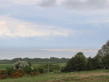 A coastal landscape with green fields trees and a body of water in the distance at The Coach House in Trelogan Hall Trelogan near Trelawnyd