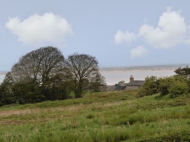 A grassy field with trees and houses near a body of water at The Coach House in Trelogan Hall Trelogan near Trelawnyd