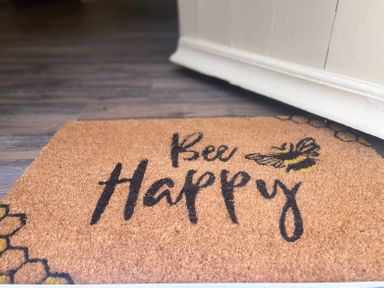 A brown doormat with the words Bee Happy and a bee design on a wooden floor at The Coach House Trelogan Hall Trelogan near Trelawnyd