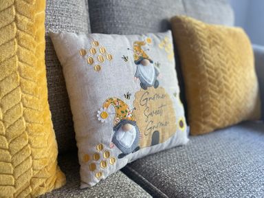 A sofa with a decorative cushion featuring gnomes and two yellow textured cushions at The Coach House in Trelogan Hall Trelogan near Trelawnyd