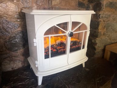 A white electric stove heater with glowing embers inside on a stone hearth at The Coach House in Trelogan Hall Trelogan near Trelawnyd