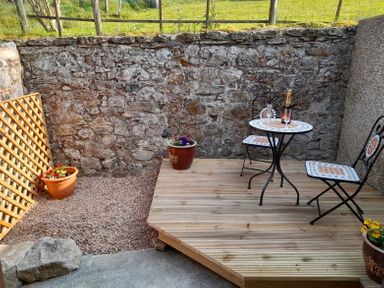 A small outdoor patio with a stone wall two chairs a table and potted plants at The Coach House in Trelogan Hall Trelogan near Trelawnyd