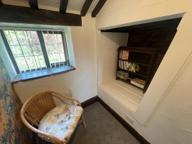A small reading nook with a rattan chair and a bookshelf in a window recess at The Coach House in Trelogan Hall Trelogan near Trelawnyd