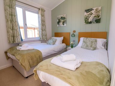 A bedroom with two single beds with green blankets and white towels at Daffodil Lodge in Mullacott near Ilfracombe