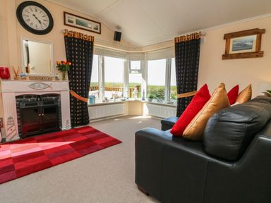 A living room with a black sofa with pillows and a white fireplace with a clock above it at Poppy Lodge in Mullacott Ilfracombe