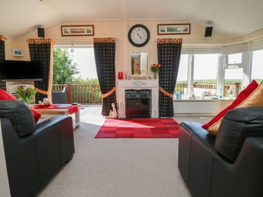 A living room with black leather sofas red pillows a red rug a fireplace and a view outside at Poppy Lodge in Mullacott Ilfracombe