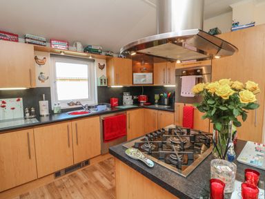 A kitchen with wooden cabinets a gas stove on a central island and yellow flowers in a vase at Poppy Lodge Mullacott Ilfracombe