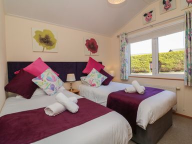 A bedroom with two single beds with pillows and rolled towels near a window at Poppy Lodge in Mullacott Ilfracombe