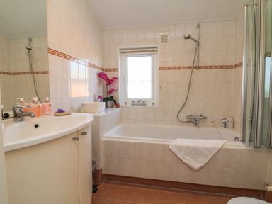 A bathroom with a bathtub shower combination a sink with toiletries and a window above the bathtub at Poppy Lodge in Mullacott Ilfracombe