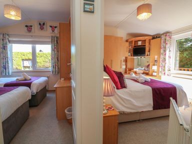 Two bedrooms with beds featuring purple runners and wooden furniture at Poppy Lodge in Mullacott Ilfracombe